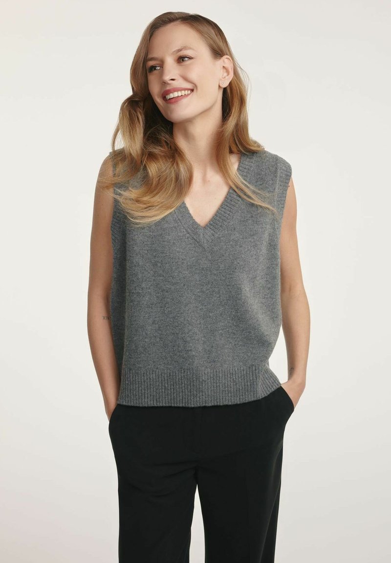 Szara bezrękawnikowa bluzka dzianinowa z dekoltem w kształcie litery V, prążkowanym dołem i miękką teksturą. Nosi się ją na czarnych spodniach, charakteryzujących się minimalistycznym wzornictwem i stonowaną kolorystyką.