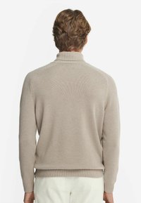 Beige stickad tröja med hög krage, ribbade manschetter och fåll. Texturen är slät med en klassisk passform och raglanärmar.