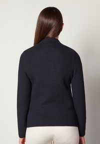 Mörk marinblå kofta med ett strukturerat stickat mönster, långa ärmar och en sjalkrage. Baksidan är figursydd och slutar strax ovanför midjan.