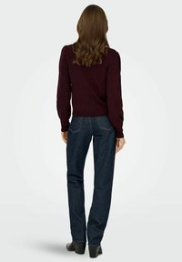 Maglione bordeaux a maglia con maniche a sbuffo, abbinato a jeans dritti blu scuro e stivali alla caviglia neri con tacco, visto da dietro.