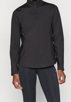 Zwart pullover met lange mouwen en een kwartritssluiting aan de voorkant, gedragen door een persoon met zichtbaar torso en armen, gecombineerd met zwarte leggings.