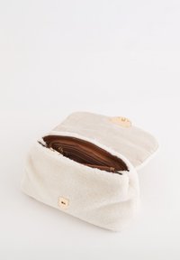 Bolso de piel sintética en color crema con textura suave, interior color cuero y herrajes dorados; cierre de cremallera con solapa plegable.