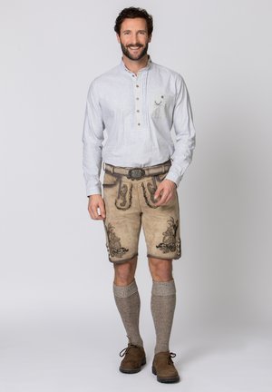 Traditionelle bayerische Tracht mit einem hellgrauen Hemd, beige Lederhosen mit schwarzer Stickerei, grauen Kniestrümpfen und braunen Schuhen.