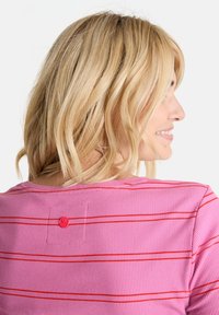 Rosa, eng anliegende Ripp-Bluse mit horizontalen roten Streifen und einem roten Knopf-Akzent auf der Rückseite.