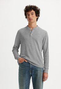 Camisa henley de manga larga gris con tres botones, fabricada en tejido acanalado texturizado y con un escote redondeado. Combinada con vaqueros de denim azules casuales.
