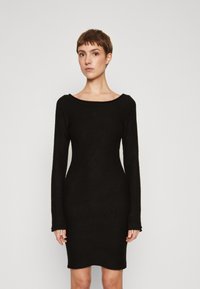 Black long-sleeve dress with a fitted silhouette, round neckline, and soft texture. The hemline is slightly curved at the bottom.