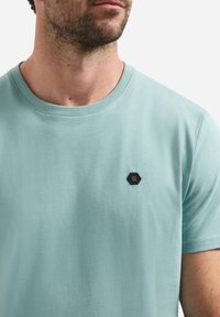 Lichtblauwe katoenen T-shirt met een ronde halslijn en korte mouwen, met een hexagonaal geborduurd logo op de linkerborst.