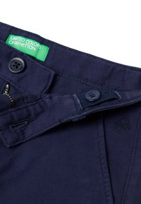 Námořnické modré bavlněné kalhoty se zipem, zapínáním na knoflík a zelenou nášivkou "United Colors of Benetton". Mají jemně strukturovanou tkaninu.