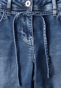 Denim-housut keskipunassa sinisessä, joissa on narukiinnitys. Ominaisuuksiin kuuluvat kontrastivärinen tikkaus, etutasku ja sileä rakenne.