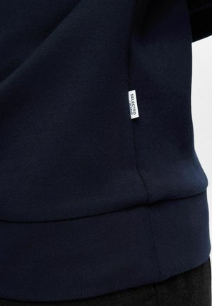 Navy blue sweatshirt with a ribbed texture, featuring a logo tag on the side. The fabric has a smooth finish and a classic design.