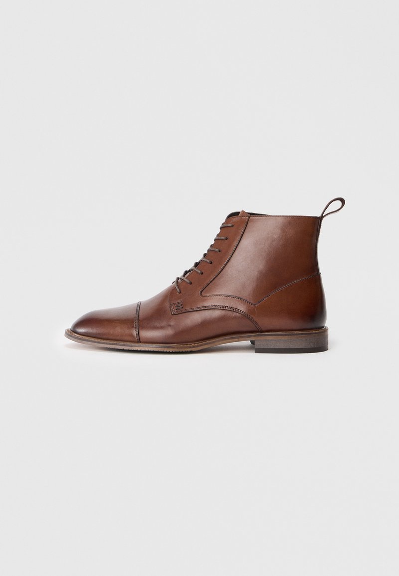Bottine en cuir marron à lacets, avec embout de cap, languette à l'arrière et petit talon en bois empilé, présentée en profil latéral sur fond blanc.
