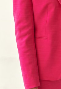 Světlý růžový blazer s texturovaným povrchem, který se vyznačuje elegantním designem, rovnými rukávy a jemným detailem přední kapsy.