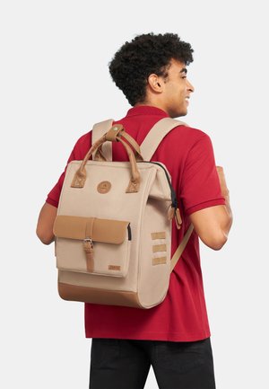 Beiger Rucksack aus Leinen mit braunen Lederakzenten, einer Frontklappen-Tasche und verstellbaren Riemen. Mit einem runden Logo und einem seitlichen Reißverschluss.