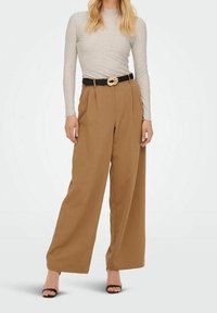 Pantalon à jambes larges en tissu beige, avec une taille haute, des plis et une ceinture noire avec une boucle dorée. Texture lisse, design structuré.