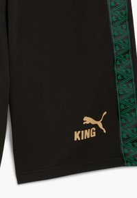 Svarta shorts med en grön texturerad sidpanel med geometriska mönster, guldtexten "KING" och en guld Puma-logga.