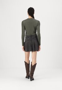 Maglietta a maniche lunghe verde scuro abbinata a una mini gonna in denim nera; stivali cowboy marroni alti fino al ginocchio con punte appuntite e dettagli texture.
