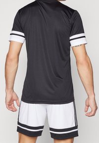 Black athletic shirt with white stripes on the sleeves, paired with white shorts featuring black accents and stripes along the hem.