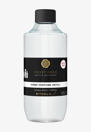 Transparante glazen fles met een zwarte dop. Heeft een zwart-witte etiket met gouden accenten, met de tekst "Velvet Oudh Home Perfume Refill."