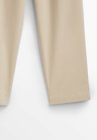 Jambes de pantalon beige montrées du milieu de la cuisse à l'ourlet sur un fond blanc, affichant une coupe droite et une texture de tissu lisse.