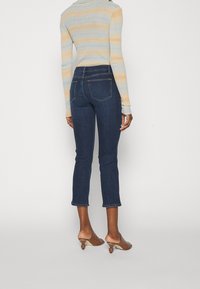 Jeans de mezclilla de color azul oscuro con un diseño ajustado, longitud recortada y bolsillos traseros cosidos. Llevados con un suéter de rayas claras y mules beiges.