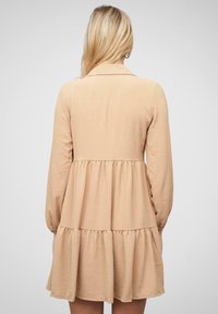 Helebeige pikkade varrukatega kleit, võrkkrae, kihiline volangääre ja pehme tekstuuriga kangas. Omab lõdva lõiget ja kogutud detaile.