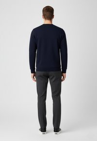 Navy Sweatshirt mit Rundhalsausschnitt und langen Ärmeln, kombiniert mit grauen Hosen. Das Outfit hat eine glatte Textur und eine figurbetonte Silhouette.