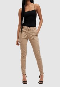 Beiga cargobyxor med tight design, flera fickor och fransad nederkant. Tillsammans med en svart tanktop och svarta sandaler med remmar.