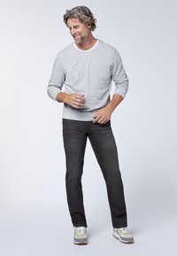 Gray long-sleeve sweatshirt with crew neckline, black jeans, and patterned sneakers. Model stands casually, smiling slightly, with hands positioned.