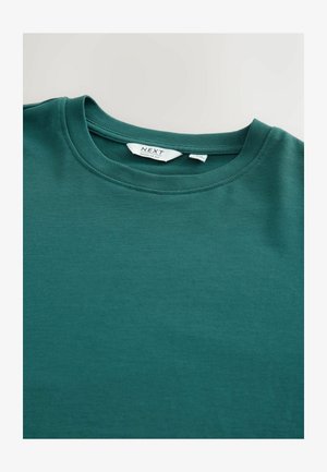 Žalia medvilninė marškinėliai su apvalia kaklo iškirpte, įprasto silueto ir lygiu paviršiumi. Etiketėje nurodytas prekės ženklas ir dydžio informacija.