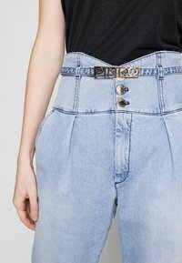 Světlé modré džíny s vysokým pasem, které mají zlatý opasek s logem "PINKO", dvě přední knoflíky a sklady v oblasti boků.