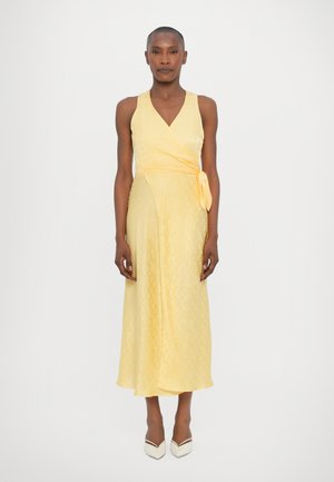 Yellow wrap dress with a v-neckline and side tie, featuring a subtle textured pattern and a flowing midi length, paired with cream heels.