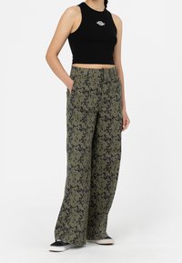 Avskuren svart linne med logotyp, kombinerat med vida olivgröna byxor med ett svart abstrakt mönster. Låga svarta och vita skor.