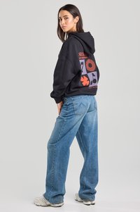 Black hoodie with graphic designs in red and purple on the back, paired with loose-fitting blue jeans and light-colored sneakers.