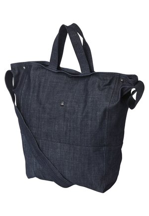 Sac cabas en denim bleu foncé avec deux poignées courtes et une longue bandoulière. Présente un tissu texturé et un détail de logo subtil.