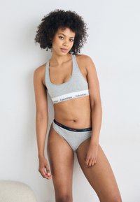 Grå bomull sport-bh med en hvit Calvin Klein-stripe og matchende gr�å stringtruse med en flerfarget logo-linning. Enkel, tettsittende design.