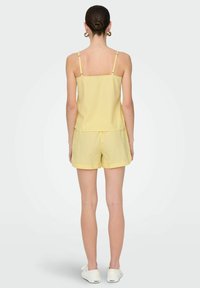 Geel gestreept mouwloos shirt gecombineerd met bijpassende shorts. De stof lijkt lichtgewicht en soepel, met dunne, verticale strepen.