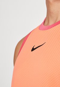 Top senza maniche Nike di un luminoso arancione con bordi rosa. Presenta una trama a rete e un piccolo logo nero sulla parte anteriore.