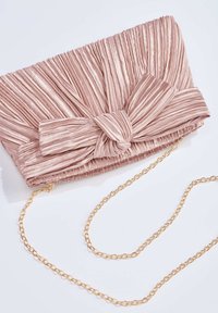 Pochette en tissu rose pâle plissé avec un grand nœud décoratif et une fine chaîne dorée sur fond blanc.