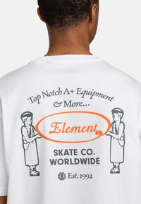 Hvid bomulds T-shirt med sort og orange grafisk print, med teksten "Top Notch A+ Equipment & More..." og illustrerede figurer, der holder et skilt.