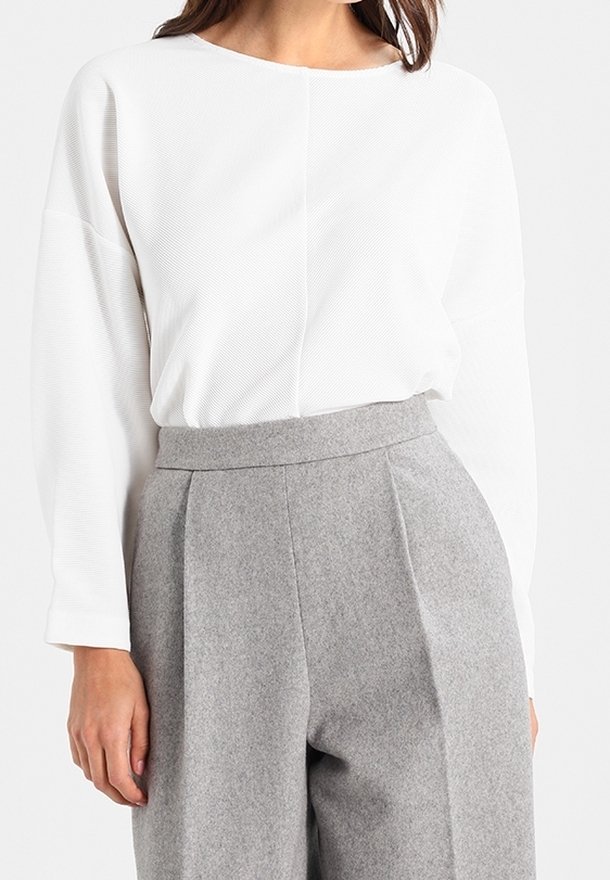 White long-sleeve top with textured fabric, paired with light grey pleated high-waist trousers made of soft wool blend.