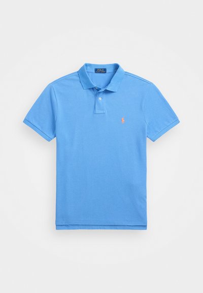 Polo de algodón en azul claro. Presenta un cuello con solapa, mangas cortas y un logo bordado en naranja en el lado izquierdo del pecho.