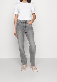 Jeans grises de talle alto con pierna recta, combinados con una camiseta blanca de cuello redondo. Los zapatos son de color marrón claro con un acabado texturizado.