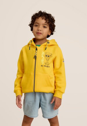 Sweat à capuche jaune avec fermeture éclair, accents en matériel bleu, poches avant, et un graphique de pizza ludique ; associé à un short en denim clair.