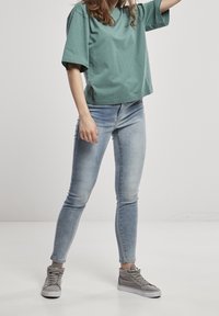 Tyrkysové bavlněné tričko s volným střihem, spárováno se světle modrými skinny džíny a šedými vysokými teniskami. Jednoduchý design, bez vzorů.