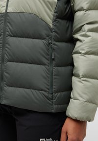 Giubbotto imbottito isolato verde scuro e verde chiaro con tasca con zip, motivo trapuntato e polsini elastici.