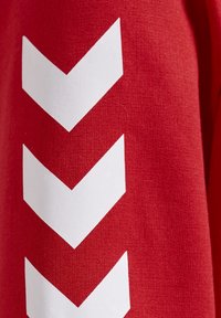 Un tejido rojo con una textura suave presenta patrones verticales en forma de flecha blanca, creando un elemento de diseño audaz en la superficie.