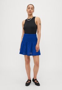 Μαύρο χωρίς μανίκια κορμάκι, συνδυασμένο με μια μπλε δαντελένια φούστα με φαρδιά τελειώματα. Μαύρα παπούτσια με λουράκι ολοκληρώνουν την εμφάνιση.