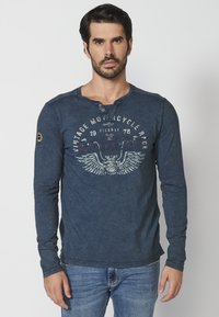 Tmavě modrá košile s dlouhým rukávem vyrobená z měkké látky, s kulatým výstřihem, detaily na knoflíky a grafickým potiskem s vintage tématem motocyklů.