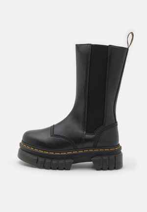 Bottine en cuir noir avec panneaux latéraux élastiques, semelle plateforme épaisse et surpiqûres jaunes le long de la semelle et des coutures.