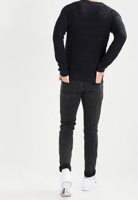 Mörk stickad tröja med ribbad textur, parat med slim fit svarta jeans och vita sneakers. Outfiten visar en avslappnad, åtsittande design.